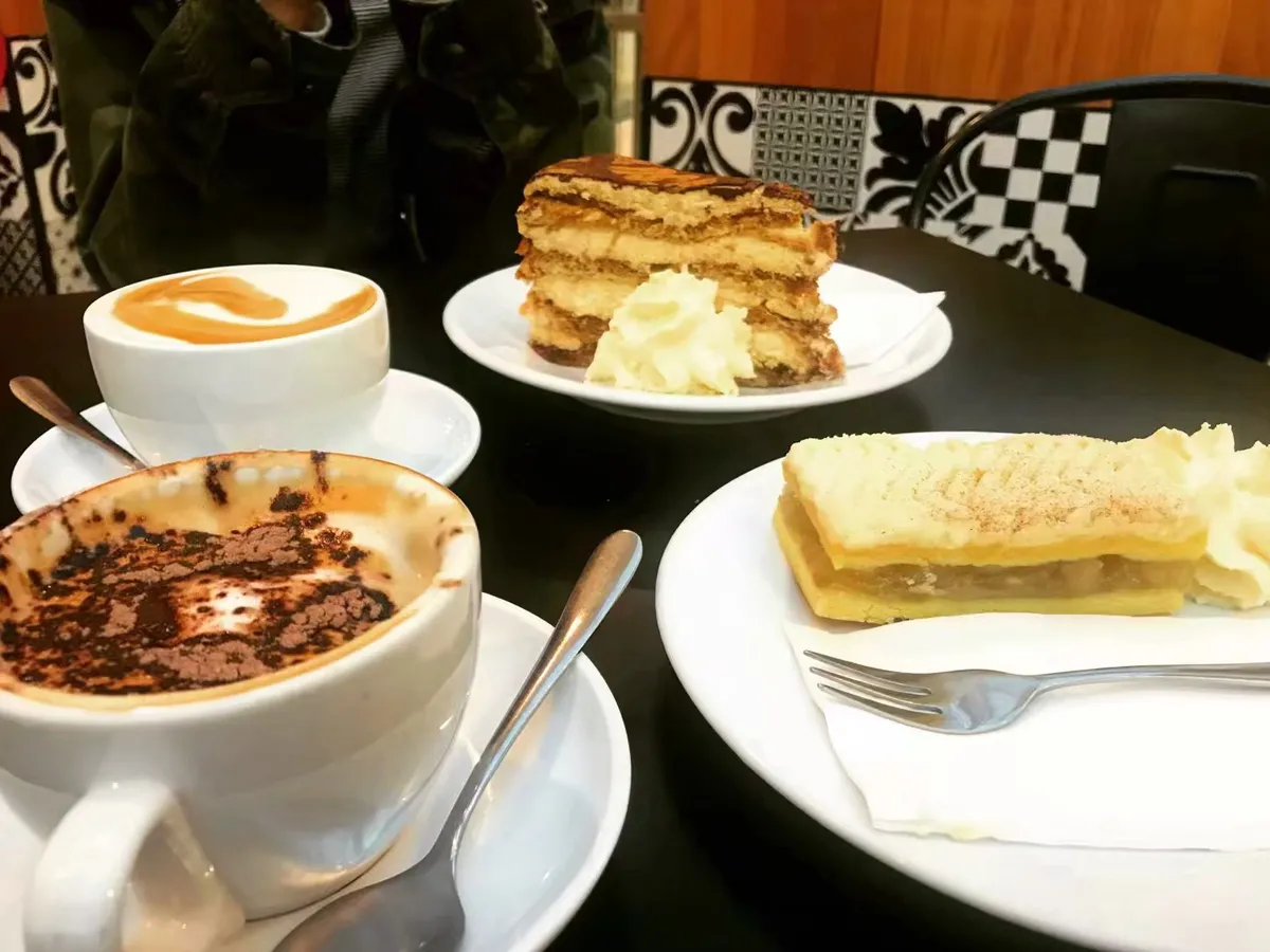 Cake slices and two cappuccinos on a table at Elly Cafe